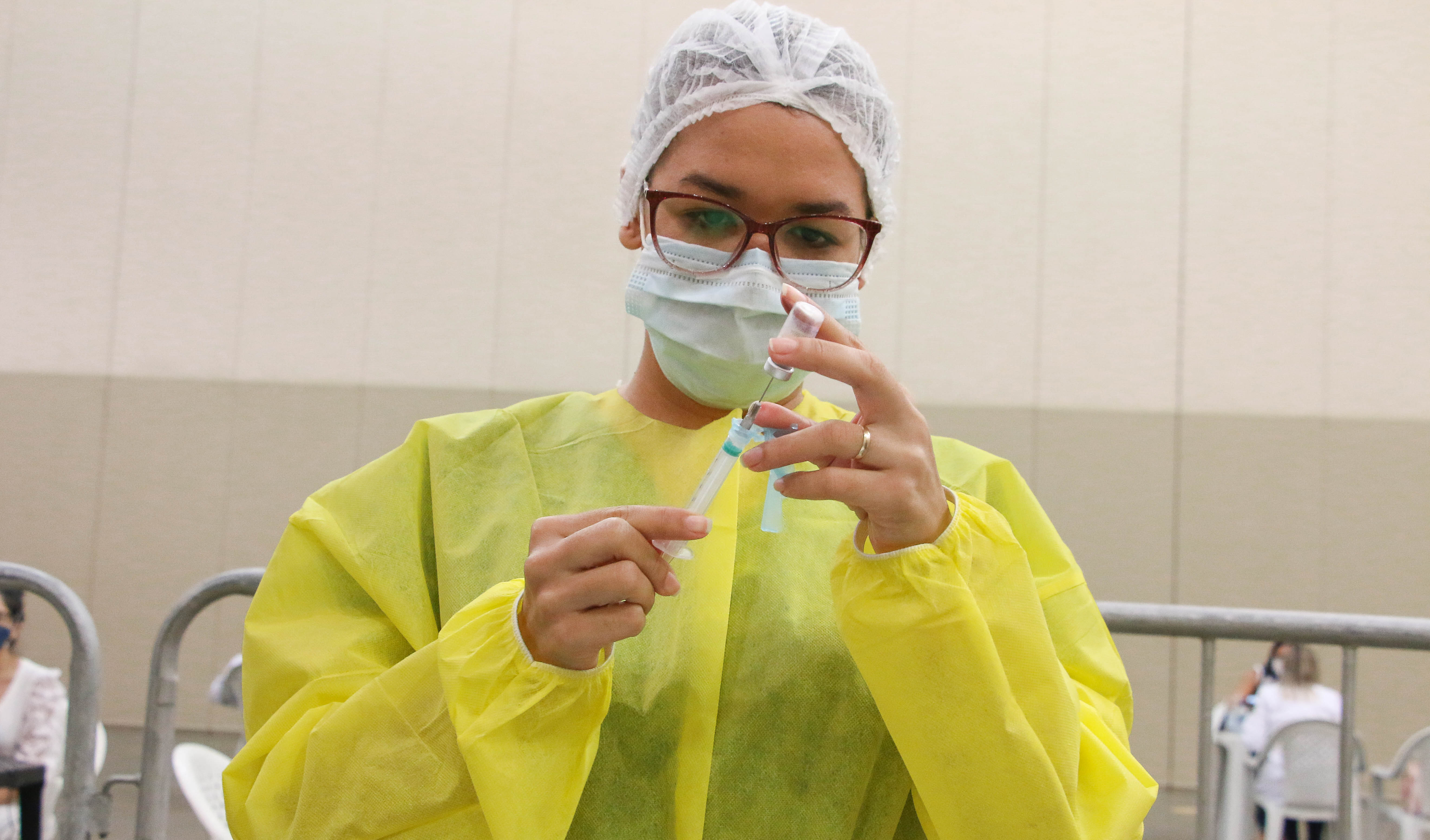enfermeira vestindo avental cirúrgico, touca e máscara manuseando seringa